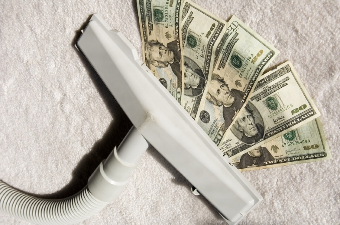 Attachment to vacuum cleaner sucking up five 20 bills on sunlit white carpet